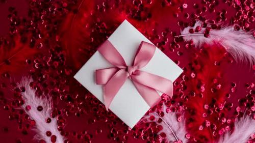 Videohive - Zoom in Out Gift Box with Pink Ribbon on Red Confetti Sequinned Background with Feathers - 42969578 - 42969578