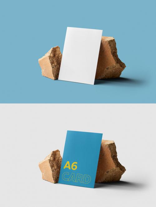 Mockup of customizable vertical color A6 card resting against rocks available against customizable color background 582960636